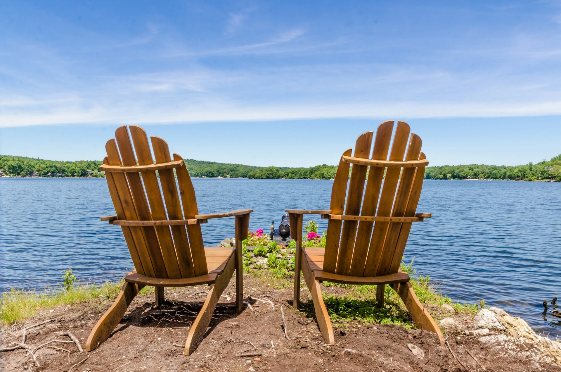 Two white adirondack chairs, looking out upon a lake